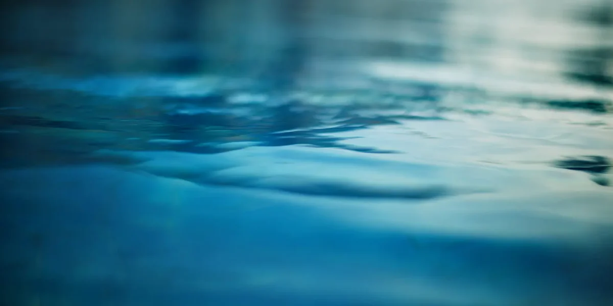 Gros plan sur une eau bleue calme avec de douces ondulations et de doux reflets, créant une atmosphère sereine et paisible.