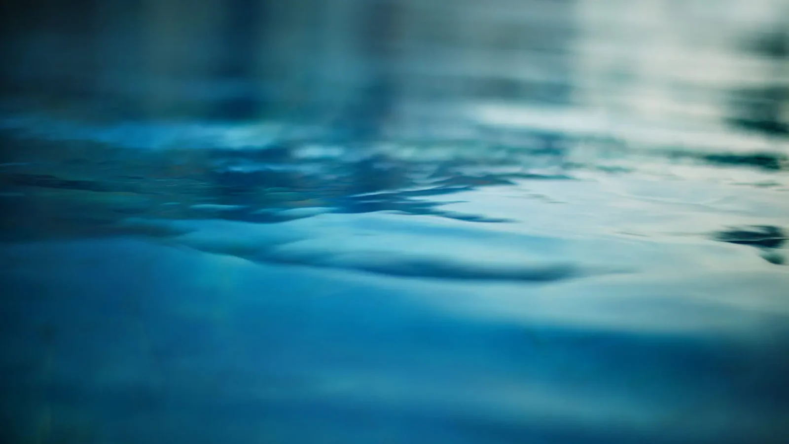 Gros plan sur une eau bleue calme avec de douces ondulations et de doux reflets, créant une atmosphère sereine et paisible.