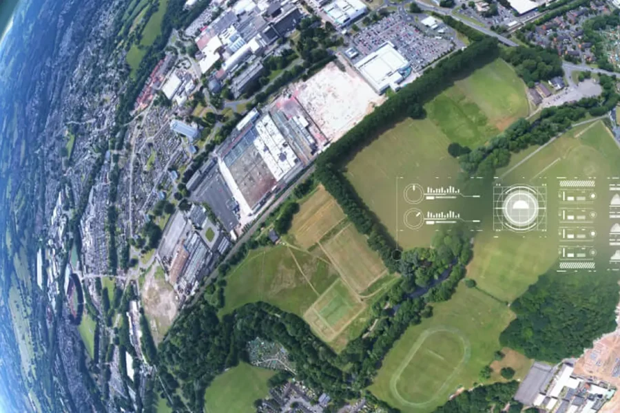 Vue aérienne d'une ville avec des champs verdoyants, des bâtiments et des zones résidentielles, le long d'un horizon incurvé, avec des données numériques et des graphiques superposés au paysage.