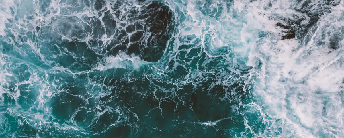 Vue aérienne de vagues océaniques turbulentes s'écrasant et tourbillonnant, créant de l'écume blanche et des motifs d'eau d'un bleu-vert profond.