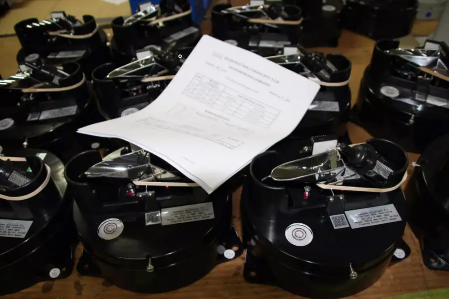 Plusieurs appareils mécaniques noirs sont disposés en rangées sur une table, un document en papier étant placé au-dessus de l'un d'entre eux. Les appareils sont munis de cadrans et de leviers, ce qui suggère qu'il s'agit d'instruments de mesure.