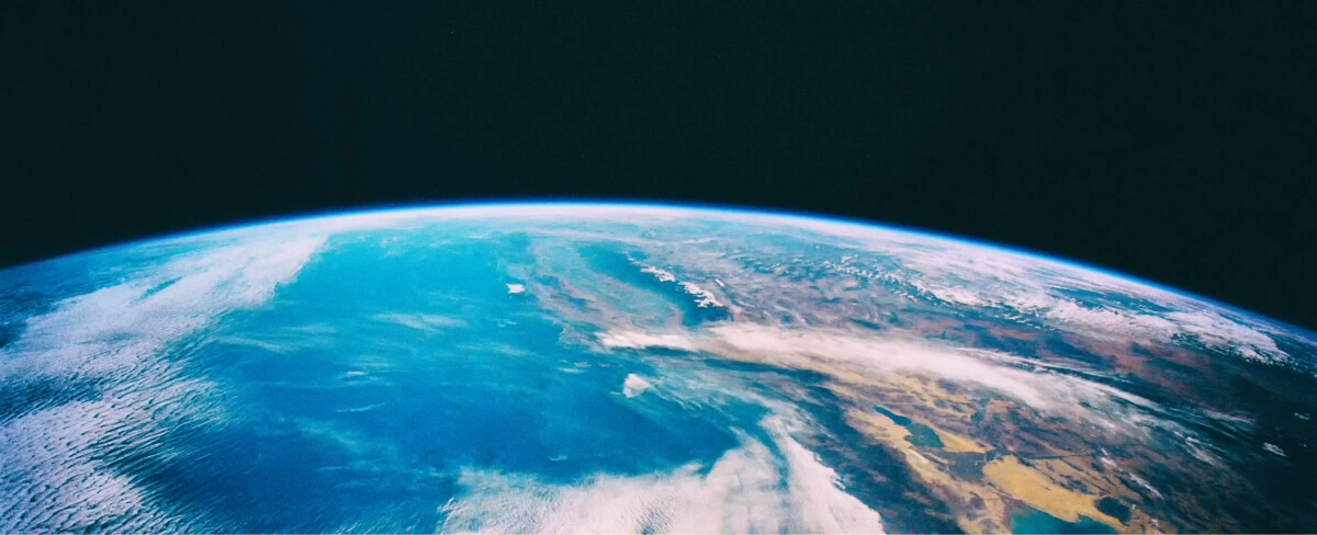 Vue de la Terre depuis l'espace montrant l'horizon incurvé de la planète, les océans bleus, les nuages blancs et les masses continentales brunes contre le noir de l'espace extra-atmosphérique.