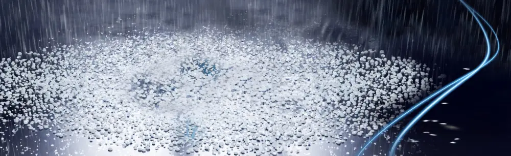 La pluie et les grêlons tombent abondamment d'un ciel sombre et nuageux sur le sol, avec quelques traînées et reflets bleu clair visibles sur le côté droit de l'image.